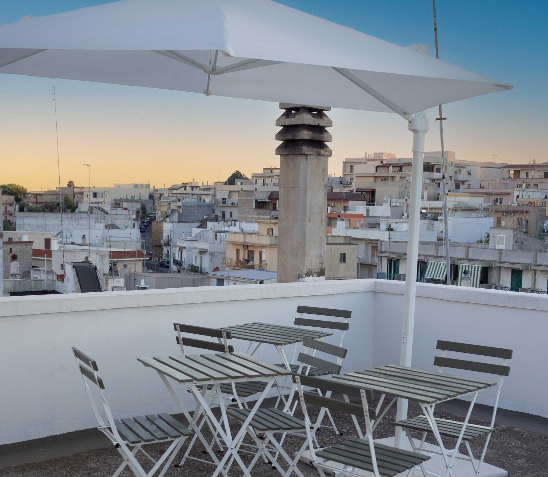 Terrazza sui tetti di Crispiano al tramonto, con tre tavoli e un ombrellone aperto