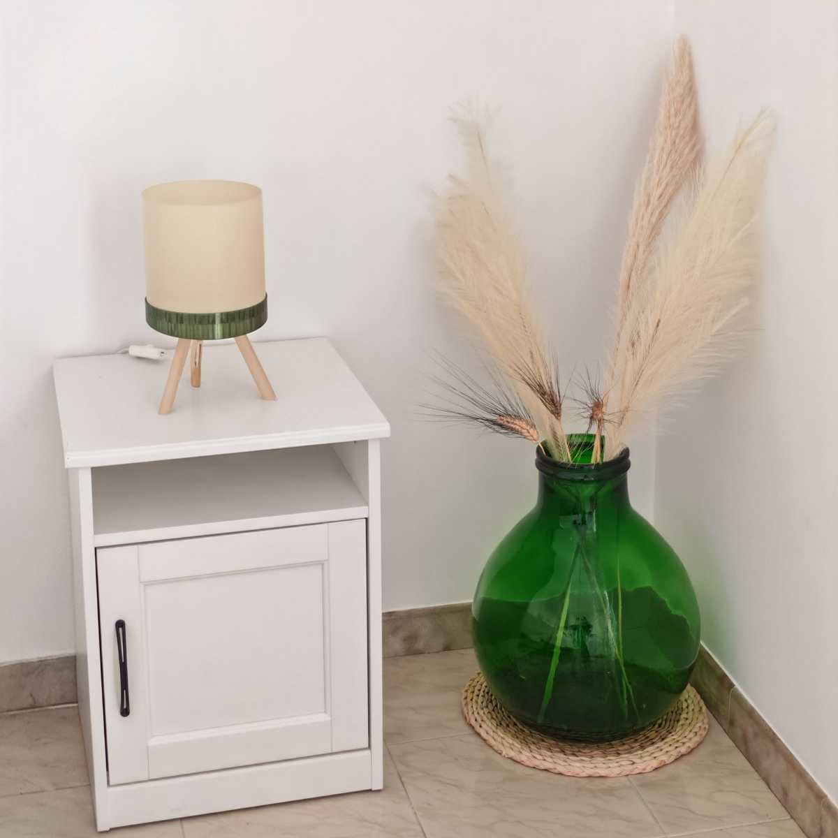 Comodino con una lampada stampata in 3D dalla base verde, accanto a una damigiana